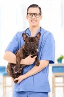 junger männlicher Tierarzt in Uniform, der einen Hund hält, drinnen