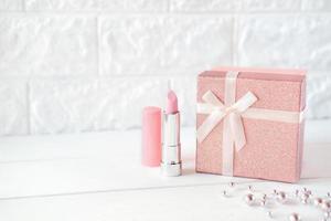rosa Lippenstift und eine Geschenkbox auf einem Tisch. rosa Halskette. foto