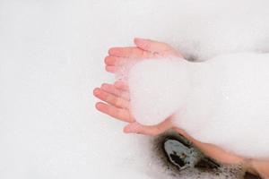 die hände des babys, die badeschaum halten. Mädchen, das Spaß im Badezimmer hat. Kind baden. Schnittansicht. Hygiene, Abendroutine foto