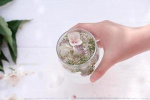 Die Hand einer jungen Frau, die ein Glas mit einem mit Blumen angereicherten Getränk hält foto