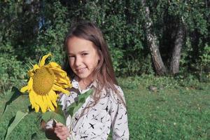 Brunettemädchen, das eine Sonnenblume hält. Sommerferien. foto