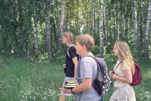 Eine Gruppe von Teenagern geht mit Rucksäcken und Büchern durch den Park zur Schule. zurück zum schulkonzept. Seitenansicht, kaukasische Teenager, Seitenansicht. blondes Haar. foto