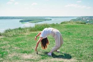 Schlanke, schöne Frau, die Yoga macht und sich im Freien dehnt. junge Frau, die allein an einem Flussufer trainiert. Person, die einen aktiven Sommerlebensstil genießt foto