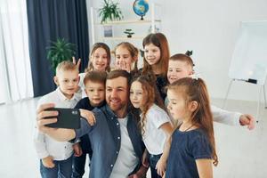 ein selfie per telefon machen. gruppe von kinderschülern im unterricht in der schule mit lehrer foto