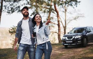 Schönheit der Natur. Paar ist mit ihrem brandneuen schwarzen Auto im Wald angekommen foto