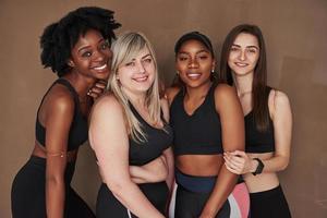 Freundschaft zwischen verschiedenen Menschen. Gruppe multiethnischer Frauen, die im Studio vor braunem Hintergrund stehen foto