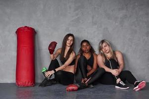 junge Boxer. Gruppe multiethnischer Frauen, die im Studio vor grauem Hintergrund sitzen foto
