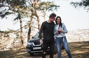 Witze machen. die Natur umarmen und genießen. Paar ist mit ihrem brandneuen schwarzen Auto im Wald angekommen foto