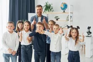 Daumen hoch zeigen. gruppe von kinderschülern im unterricht in der schule mit lehrer foto