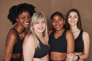 Nahaufnahme Foto. Gruppe multiethnischer Frauen, die im Studio vor braunem Hintergrund stehen foto