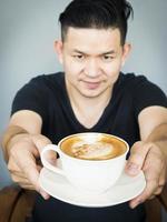 asiatischer mann, der heiße kaffeetasse zeigt foto