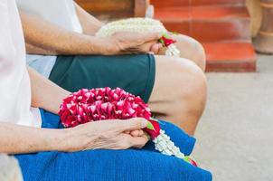 alte weibliche Hand mit Rosengirlande und verschwommene alte männliche Hand mit Jasmingirlande. thailändische Tradition für besondere Familienanlässe, bei denen jüngere Familienmitglieder entsprechend hoch zahlen. foto