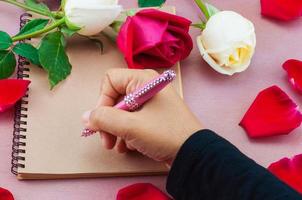 Frauenhand bereit, ein Notizbuch mit roter und weißer Rosendekoration zu schreiben foto