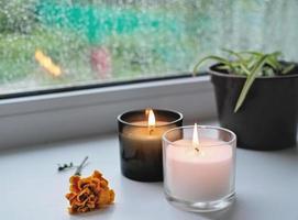 brennende Kerzen und orangefarbene Herbstblumen auf einer Fensterbank. Regentag und Tropfen auf einem Fenster. herbstmorgenkonzept, hygge house.