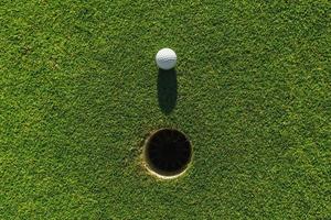 Golfball auf grünem Gras mit Loch und Sonnenlicht foto