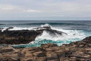 turbulente Meereswellen mit weißem Schaum schlagen Küstensteine foto