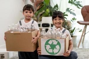 lächelnde kinder, die spaß haben, während sie plastikflaschen und papier in einen behälter trennen foto