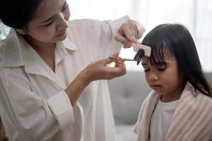 asiatische mutter schneidet ihrer tochter im wohnzimmer zu hause die haare, während sie während der sperrung zu hause sicher vor dem covid-19-coronavirus bleibt. selbstquarantäne und soziales distanzierungskonzept. foto