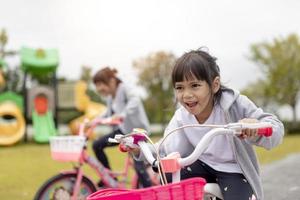 Fröhliches, fröhliches Mädchen, das im Park in der Natur Fahrrad fährt foto