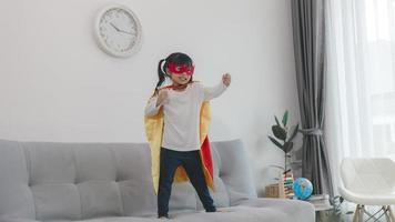 Kindermädchen in einem Superheldenkostüm mit Maske und rotem Umhang zu Hause foto