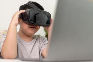 asiatischer kleiner junge mit vr-brille, der zu hause naturwissenschaften studiert, neugieriger student trägt ein virtual-reality-headset, um naturwissenschaften zu hause online zu studieren, futuristischer lebensstil lernen foto