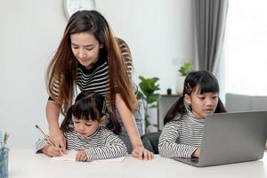 asiatisches kleines junges mädchen, das zu hause mit der mutter online-unterricht lernt. vorschulkind benutzt laptop-computer, macht hausaufgaben, homeschool vom schullehrer über digitales remote-internet mit unterstützung von mama. foto