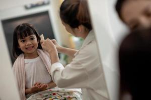 asiatische mutter schneidet ihrer tochter im wohnzimmer zu hause die haare, während sie während der sperrung zu hause sicher vor dem covid-19-coronavirus bleibt. selbstquarantäne und soziales distanzierungskonzept. foto