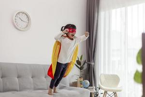 Kindermädchen in einem Superheldenkostüm mit Maske und rotem Umhang zu Hause foto