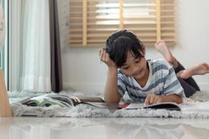 Kinderlesebuch zu Hause. Mädchen, das drinnen liegt und liest foto