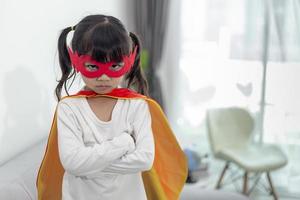 Kindermädchen in einem Superheldenkostüm mit Maske und rotem Umhang zu Hause foto