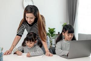 asiatisches kleines junges mädchen, das zu hause mit der mutter online-unterricht lernt. vorschulkind benutzt laptop-computer, macht hausaufgaben, homeschool vom schullehrer über digitales remote-internet mit unterstützung von mama. foto