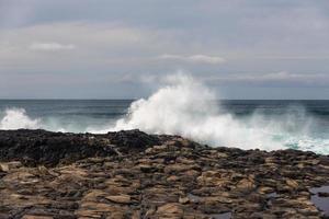 turbulente Meereswellen mit weißem Schaum schlagen Küstensteine foto