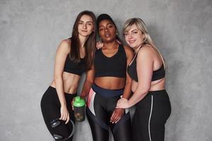 Nahrungsergänzungsmittel immer wichtig vor und nach dem Training. Gruppe multiethnischer Frauen, die im Studio vor grauem Hintergrund stehen foto