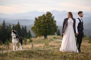 Fröhliche stilvolle Braut und Bräutigam, die an sonnigen Sommertagen in den Bergen laufen und Spaß haben foto