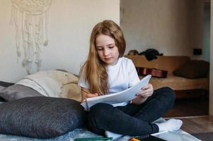 das mädchen nach der schule spielt zu hause, zeichnet mit bleistiften und filzstiften foto