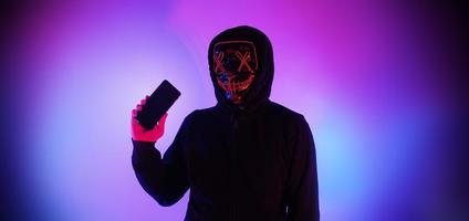 Anonymer Hacker und Gesichtsmaske mit Smartphone in der Hand. foto