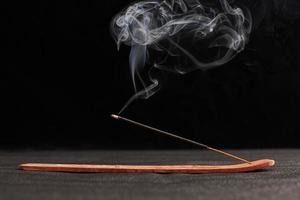 Rauchlocken aus brennendem Räucherstäbchen in Holzhalter für Entspannung und Meditation auf schwarzem Hintergrund foto