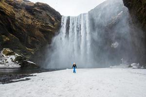 Tourist steht während der Wintersaison vor Skogafoss, einem der bekanntesten Wasserfälle in Südisland. foto