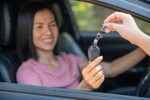 Eine attraktive Frau in einem Auto bekommt die Autoschlüssel. miete oder kauf von auto - konzept. professioneller verkäufer während der arbeit mit kunden im autohaus. Schlüsselübergabe an Neuwagenbesitzer. foto