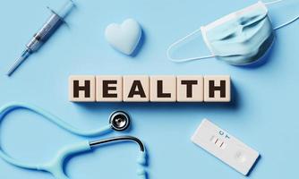Gesundheit hölzerne Wortblockwürfel mit medizinischer Ausrüstung auf blauem Papierhintergrund. gesundheitswesen und gesundes konzept. 3D-Darstellungswiedergabe foto