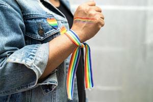 asiatische dame mit regenbogenflaggenarmbändern, symbol des lgbt-stolzmonats, feiert jährlich im juni die sozialarbeit von schwulen, lesbischen, bisexuellen, transgendern und menschenrechten. foto