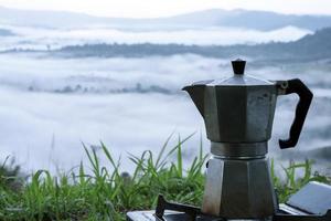 Moka-Kaffeekanne auf grünem Gras mit Tautropfen Der Hintergrund ist ein nebliger Berg. foto