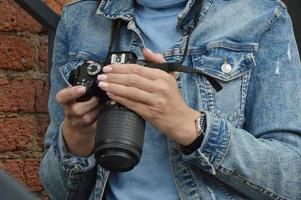 Frauenhände halten eine Kamera. ein mädchen in einer jeansjacke sieht sich bilder auf einer professionellen kamera an. Nahansicht. foto