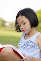 Asiatisches kleines Mädchen liest Buch im Park foto