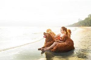 glückliche junge frau, die ihre hunde am strand bei sonnenuntergang übt foto