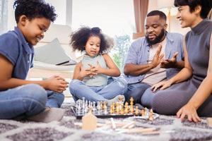 Zwei afroamerikanische Kinder mit Mutter und Vater spielen eine Partie Schach und haben gemeinsam Spaß foto