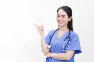 Eine schöne junge asiatische Ärztin in blauer Uniform steht und lächelt, während sie auf einem weißen Hintergrund nach oben zeigt. foto