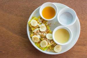 Das Roti mit Bananenscheiben wurde mit gesüßtem Kondensmilchzucker und Bananensoße serviert, darüber Mandelscheiben auf einem weißen Teller. foto