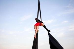 Übungen mit Luftseide im Freien, Himmelshintergrund. schöne fitte frau, die akrobatik in der luft trainiert. foto