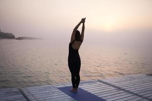 junge frau, die in yoga-asans, morgenseehintergrund aufwirft foto